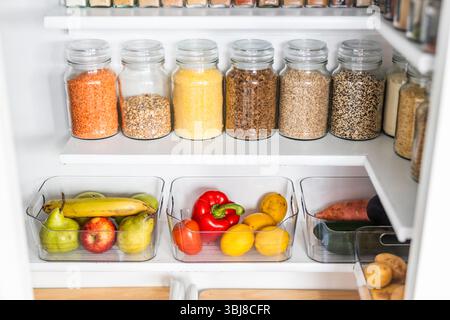 petit garde-manger organisé avec des bocaux transparents assortis remplis de céréales, légumineuses, épices et produits frais dans des récipients, alimentation saine, maison rangée, organi Banque D'Images