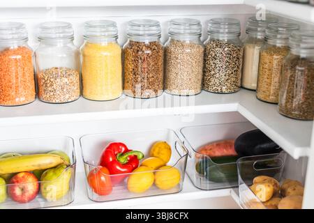 petit garde-manger organisé avec des bocaux transparents assortis remplis de céréales, légumineuses, épices et produits frais dans des récipients, alimentation saine, maison rangée, organi Banque D'Images