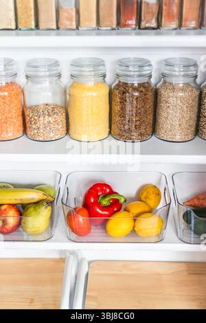 petit garde-manger organisé avec des bocaux transparents assortis remplis de céréales, légumineuses, épices et produits frais dans des récipients, alimentation saine, maison rangée, organi Banque D'Images