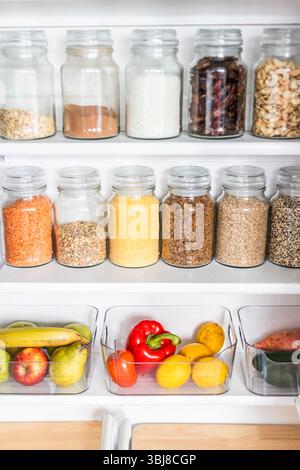 petit garde-manger organisé avec des bocaux transparents assortis remplis de céréales, légumineuses, épices et produits frais dans des récipients, alimentation saine, maison rangée, organi Banque D'Images
