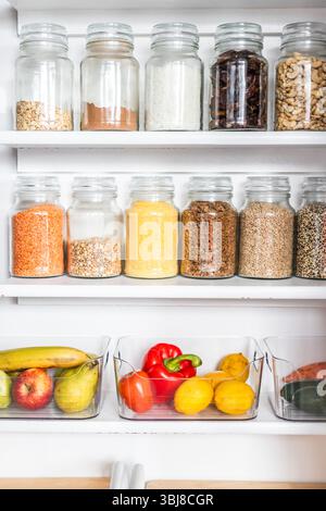 petit garde-manger organisé avec des bocaux transparents assortis remplis de céréales, légumineuses, épices et produits frais dans des récipients, alimentation saine, maison rangée, organi Banque D'Images