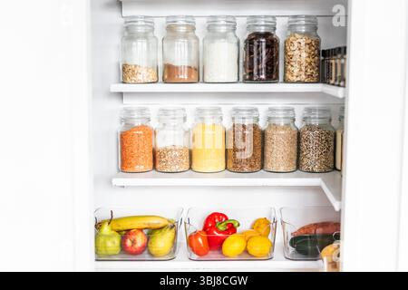 petit garde-manger organisé avec des bocaux transparents assortis remplis de céréales, légumineuses, épices et produits frais dans des récipients, alimentation saine, maison rangée, organi Banque D'Images