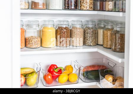 petit garde-manger organisé avec des bocaux transparents assortis remplis de céréales, légumineuses, épices et produits frais dans des récipients, alimentation saine, maison rangée, organi Banque D'Images