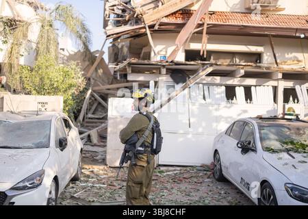 Rishon LeZion, Israël. 14 juin 2025. Un membre des Forces armées israéliennes (FDI) se tient devant des bâtiments endommagés après qu'un missile iranien a frappé Rishon Lezion, tuant au moins deux personnes et en blessant plusieurs autres. Crédit : Ilia Yefimovich/dpa/Alamy Live News Banque D'Images