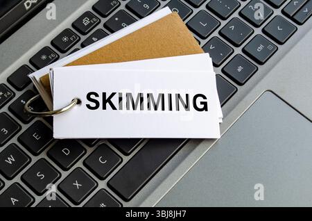 Skimming texte sur bloc-notes blanc avec fond de clavier d'ordinateur portable. Concept d'activité hacker et arnaque Banque D'Images