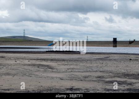 Les bas niveaux d'eau au réservoir Warland révèlent un cadre de bateau coulé, avec des pylônes et des structures lointains. Banque D'Images