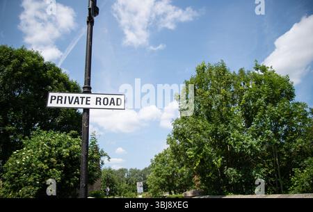 Panneau routier privé avec texte blanc sur fond noir, placé sur un fond d'arbres verts luxuriants sur une route rurale tranquille. Banque D'Images