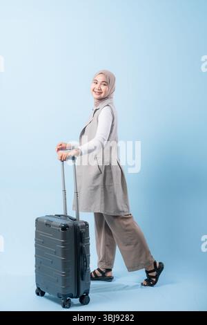 Une femme tient une valise et sourit. La valise est argentée et a des roues. La femme porte une chemise blanche et une écharpe. Concept de voyage et Banque D'Images