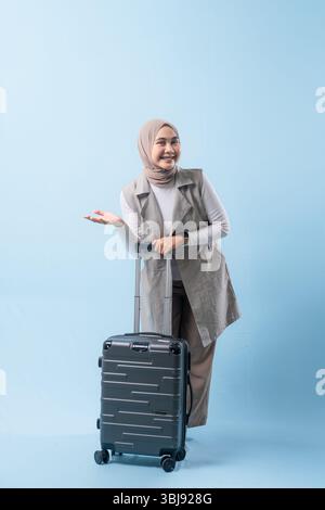 Une femme tient une valise et sourit. La valise est argentée et a des roues. La femme porte une chemise blanche et une écharpe. Concept de voyage et Banque D'Images