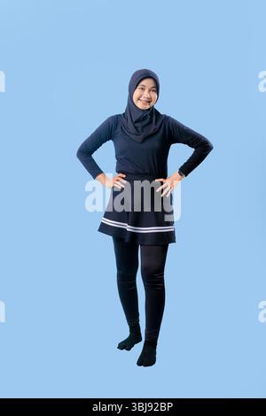 Une femme portant une jupe noire et un pantalon noir. Elle sourit. L'arrière-plan est bleu. La femme est debout devant un mur Banque D'Images