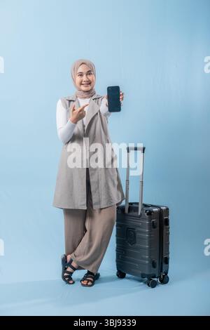 Une femme tient un téléphone portable noir et pointe vers lui. Elle sourit et elle est heureuse Banque D'Images