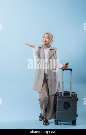 Une femme portant une chemise blanche et un gilet gris tient une valise et pointe vers quelque chose d'important Banque D'Images
