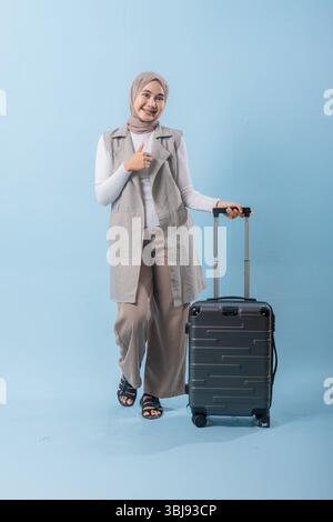 Une femme portant un foulard tient un téléphone portable et sourit. Elle est debout près d'une valise Banque D'Images