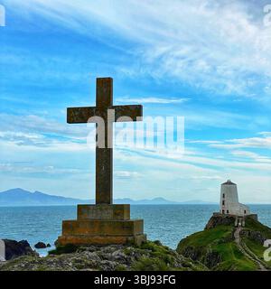 Croix de pierre sur Ynys Llandwyn avec phare et montagnes de Snowdonia à distance sous ciel bleu vif et nuages blancs tortueux Banque D'Images
