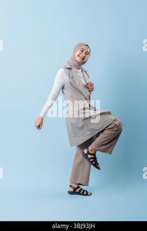 Une femme portant un gilet gris et une chemise blanche sourit à la caméra. Elle porte un foulard et a les bras croisés Banque D'Images