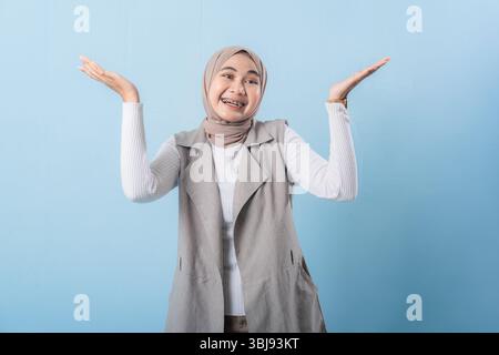 Une femme portant un gilet gris et une chemise blanche sourit à la caméra. Elle porte un foulard et a les bras croisés Banque D'Images