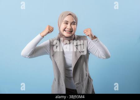 Une femme dans un gilet gris sourit et lève les bras. Elle porte un foulard et elle est heureuse Banque D'Images