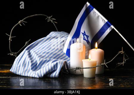 Uniforme de prisonnier, bougies allumées, fil de fer barbelé et drapeau d'Israël sur fond sombre. Jour du souvenir de l'Holocauste Banque D'Images