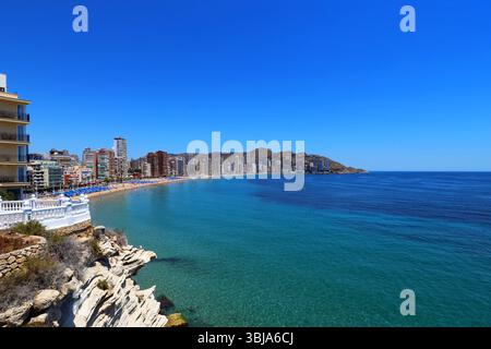 Vue panoramique sur la côte de Benidorm, Espagne, avec des eaux turquoises, plage de sable, gratte-ciel, et le ciel bleu de Balcón del Mediterráneo rocheux. Banque D'Images