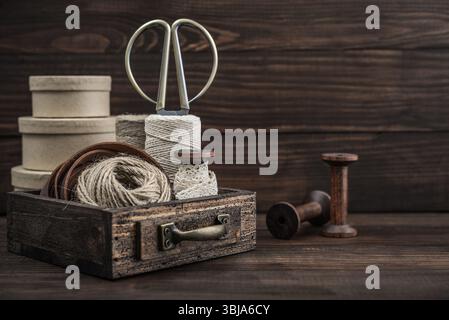 Outils et accessoires pour l'artisanat ou l'emballage cadeau : ciseaux de bonsaï, corde de jute, ruban de cuir et bobines dans une boîte en bois vintage sur BA en bois foncé Banque D'Images