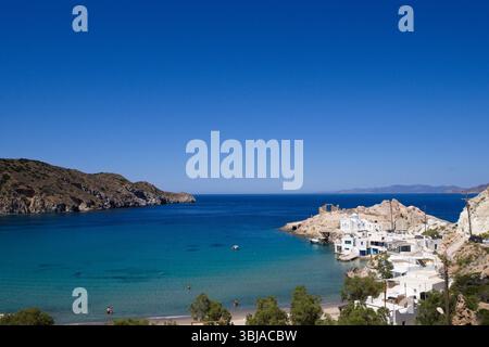 Vue panoramique lointaine de la baie de Firopotamos sur Milos avec des maisons des Cyclades, une mer turquoise calme et un ciel bleu clair sur une journée d'été tranquille. Banque D'Images