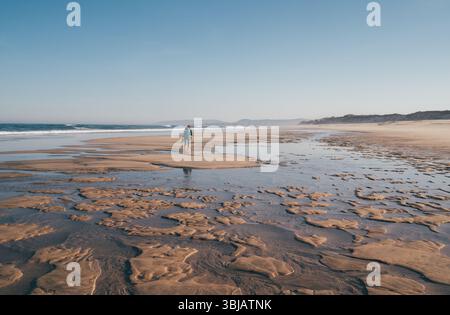 Femme solitaire marchant par une large plage de sable à marée basse et longue et profitant des vagues de l'océan Atlantique au Portugal. Tourné pendant le Camino Portugais — populaire pil Banque D'Images