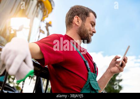 Ouvrier agricole souriant à l'aide d'un smartphone près de la moissonneuse-batteuse Banque D'Images