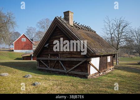 Un chalet traditionnel en bois avec un toit de chaume distinctif et une cheminée en briques se dresse sur une colline herbeuse à Hässleholm, en Suède. Banque D'Images