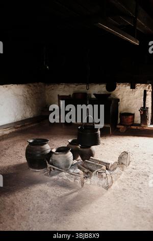 Pot noir traditionnel et batterie de cuisine en argile autour d'un foyer en pierre dans une ancienne maison rurale serbe. Village ethno Staro Selo. Banque D'Images