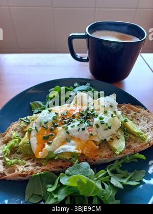 Pain grillé sain à l'avocat ouvert garni d'oeuf liquide et de ciboulette servi sur du pain au levain avec de la roquette et une tasse de café noir Banque D'Images