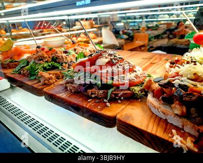 Assortiment de sandwichs ouverts recouverts d'ingrédients comme le thon, la tomate, le saumon, le fromage et les graines sur du pain rustique, présentés sur des planches de bois à l'intérieur d'un puits Banque D'Images