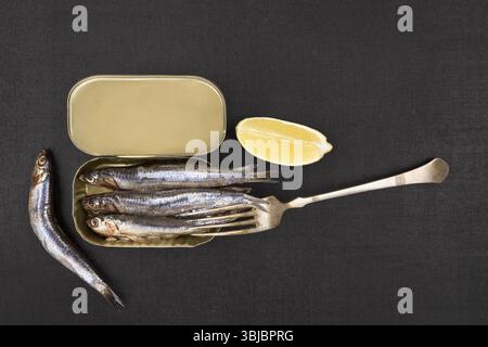 Boîte ouverte avec sardines et morceau de citron isolé sur fond texturé noir, vue de dessus. Fruits de mer culinaires Banque D'Images
