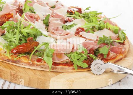 Pizza culinaire avec prosciutto, tomates sèches et herbes fraîches sur planche à découper en bois sur table en bois Banque D'Images