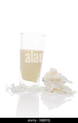 Lait de coco en verre avec des flocons de noix de coco dans un bol en verre isolé sur fond blanc. Concept de lait végétalien et végétarien Banque D'Images