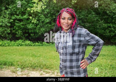 Jeune femme noire confiante avec une coiffure protectrice colorée portant une chemise à carreaux à l'extérieur, parfaite pour le style de vie et le contenu de diversité Banque D'Images