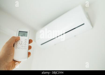 Main tenant la télécommande dirigée vers le climatiseur Banque D'Images