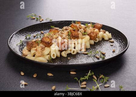 Délicieuses pâtes aux pois chiches, tofu frit et herbes fraîches sur assiette noire. Nourriture végétalienne Banque D'Images