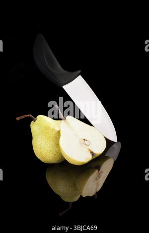 Poire avec couteau en céramique isolé sur fond noir avec réflexion. Fruits en noir luxueux Banque D'Images