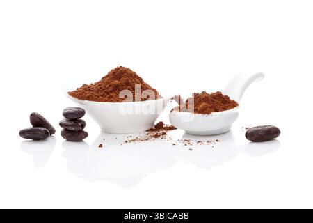 Fèves de cacao et poudre de cacao dans un bol blanc et cuillère blanche sur fond blanc. Super-aliment sain Banque D'Images