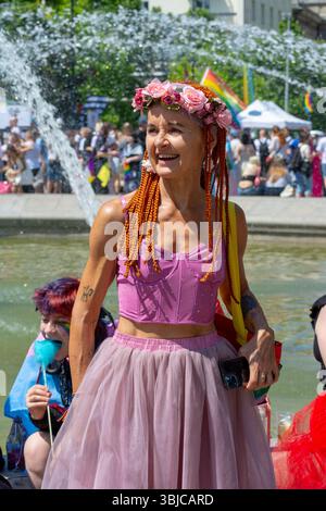 Une femme portant une couronne de fleurs et un tutu rose sourit près d'une fontaine lors de la Parade de la fierté de Varsovie au jardin saxon, Varsovie, Pologne, en juin 2025. Banque D'Images