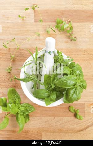 Herbes aromatiques culinaires fraîches basilic, thym et romarin dans le mortier avec pilon sur fond de bois. Vue de dessus Banque D'Images