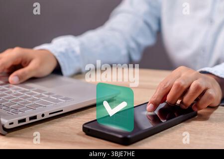Une femme d'affaires utilisant un smartphone avec une coche verte sur l'écran. Concept validé, confirmé, complété, approuvé et vérifié. Banque D'Images