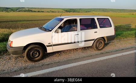 10.05.2025 Moldavie Un charmant VUS compact blanc vintage est garé gracieusement sur une route rurale pittoresque au milieu de la campagne pittoresque Banque D'Images