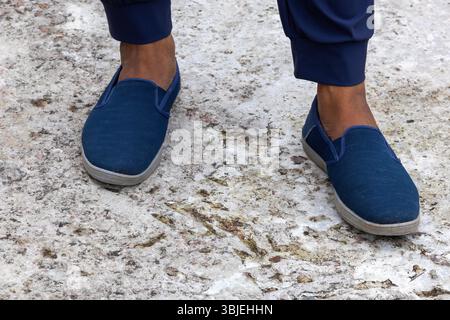 Pied masculin en baskets bleu marine sur béton. Chaussures confortables à la mode élégantes, chaussures pour hommes rapprochées. Banque D'Images