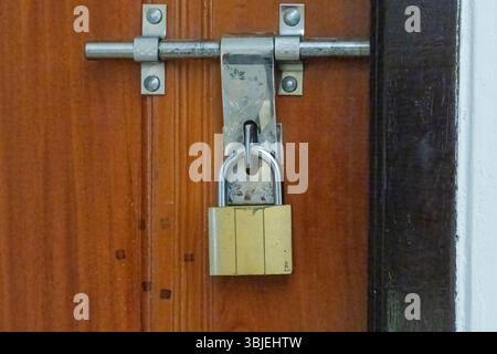 Cadenas doré verrouillé sur une porte en bois avec loquet en acier inoxydable. Banque D'Images