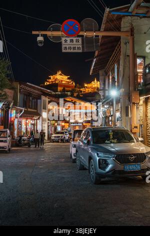 Shangri-la, Chine - 20 octobre 2024 : des bâtiments illuminés et des voitures garées bordent une charmante rue dans la ville antique de Dukezong la nuit. Banque D'Images