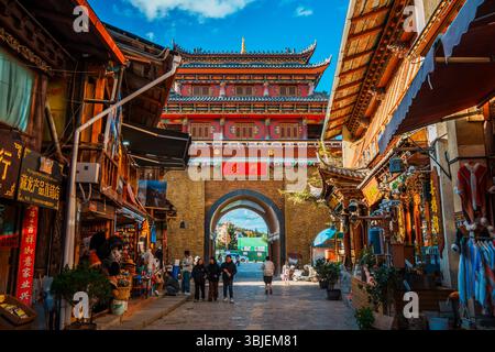 Shangri-la, Chine - 20 octobre 2024 : les touristes traversent l'arche traditionnelle de la ville antique de Dukezong sous un ciel bleu clair. Banque D'Images