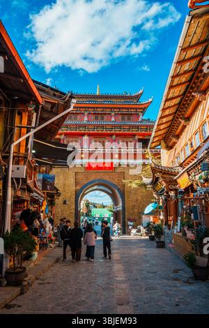 Shangri-la, Chine - 20 octobre 2024 : les touristes traversent l'arche traditionnelle de la ville antique de Dukezong sous un ciel bleu clair. Banque D'Images
