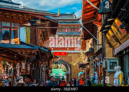 Shangri-la, Chine - 20 octobre 2024 : les touristes traversent l'arche traditionnelle de la ville antique de Dukezong sous un ciel bleu clair. Banque D'Images