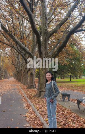 Une femme chinoise heureuse debout sur un trottoir près de feuilles de sycomore tombées dans Flushing Meadows Corona Park dans le Queens New York à la fin de l'automne. Banque D'Images